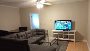A living room with a sectional sofa, a glass coffee table, a flat-screen TV on a white stand, and a ceiling fan. - Great Apartment in Historic Downtown Columbus. (Columbus)