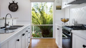 A kitchen with white cabinetry, a sink, a stove, and a window overlooking greenery. - Aggies Way - dog friendly with  panoramic views (Daylesford)