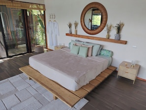 Ein Schlafzimmer mit einem großen Bett, einer hölzernen Bank, einem Nachttisch, einem Regal mit Pflanzen und einem Spiegel.
