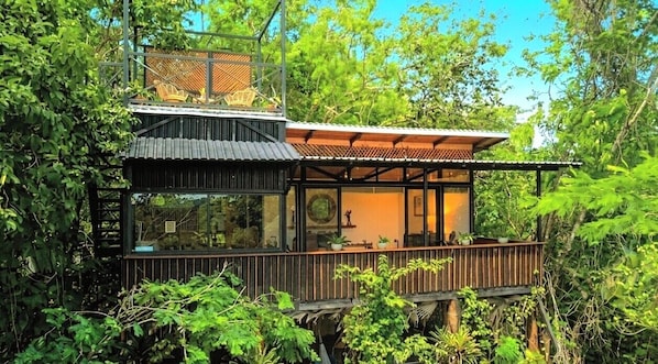 Ein modernes Haus mit Holzterrasse, großen Fenstern und Blick ins grüne Umland.