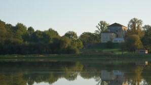 A house by a calm lake with a clear reflection, surrounded by trees and greenery.