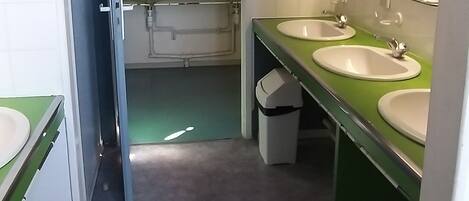 A narrow bathroom with two sinks, a trash bin, and a mirror.