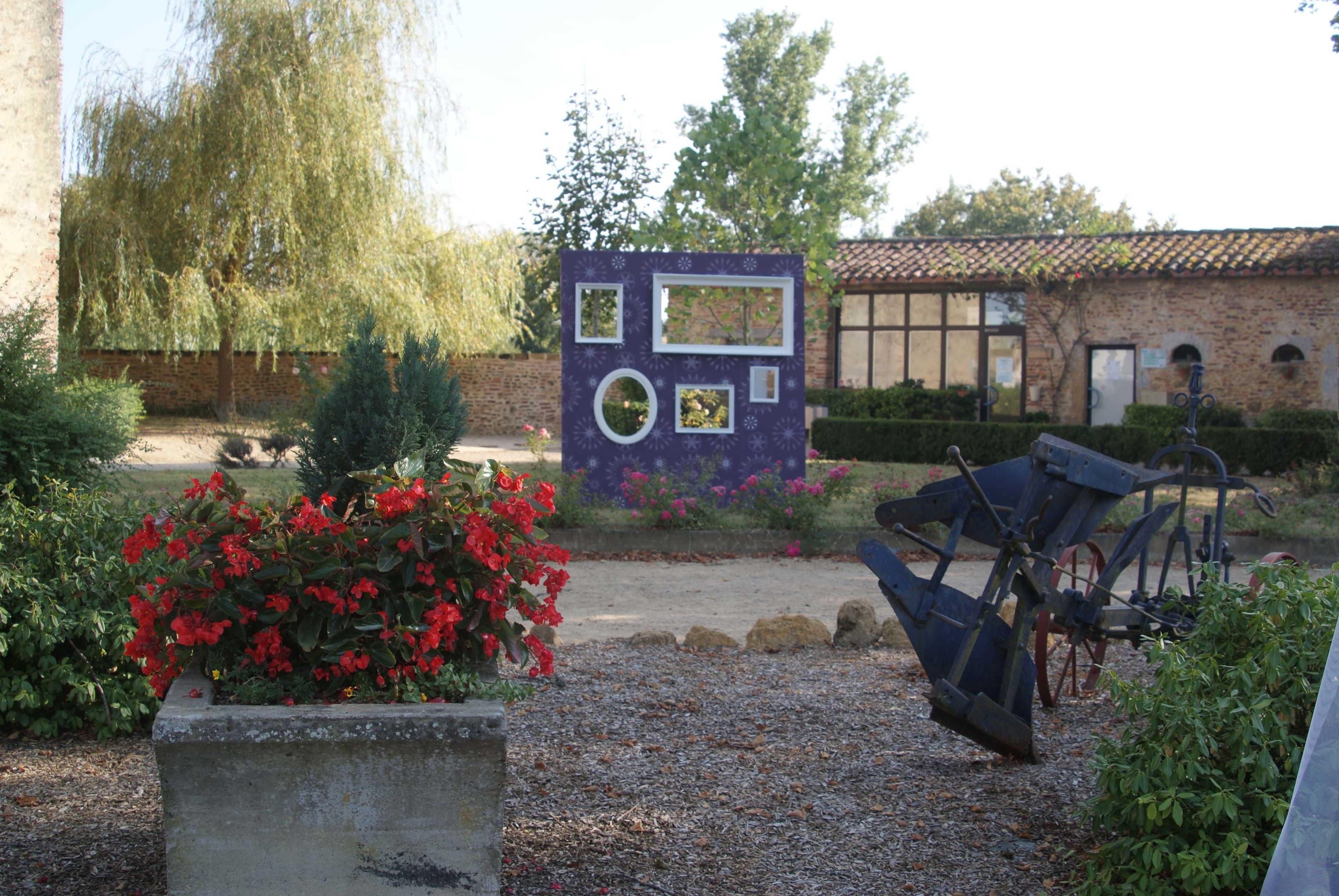 A garden with a decorative structure, a tractor, and a brick building in the background.