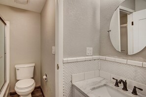 A bathroom with a toilet, a sink with two faucets, and a mirror above the sink. - 2bd_mw_315 (Frisco)