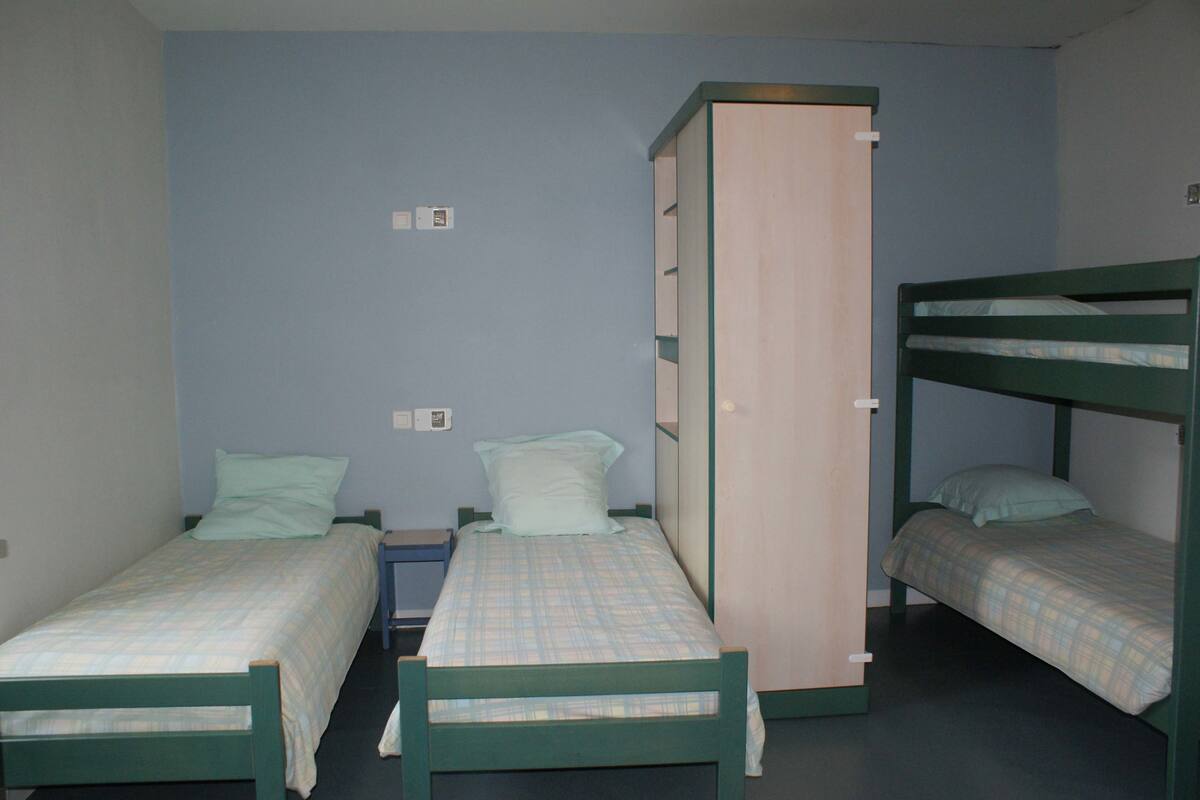 A dormitory room with three bunk beds and a single bed, each with a plaid bedspread.