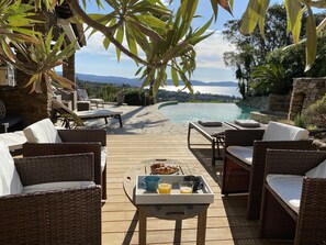 A wooden deck with wicker furniture, a breakfast tray, and a view of a swimming pool and mountains.