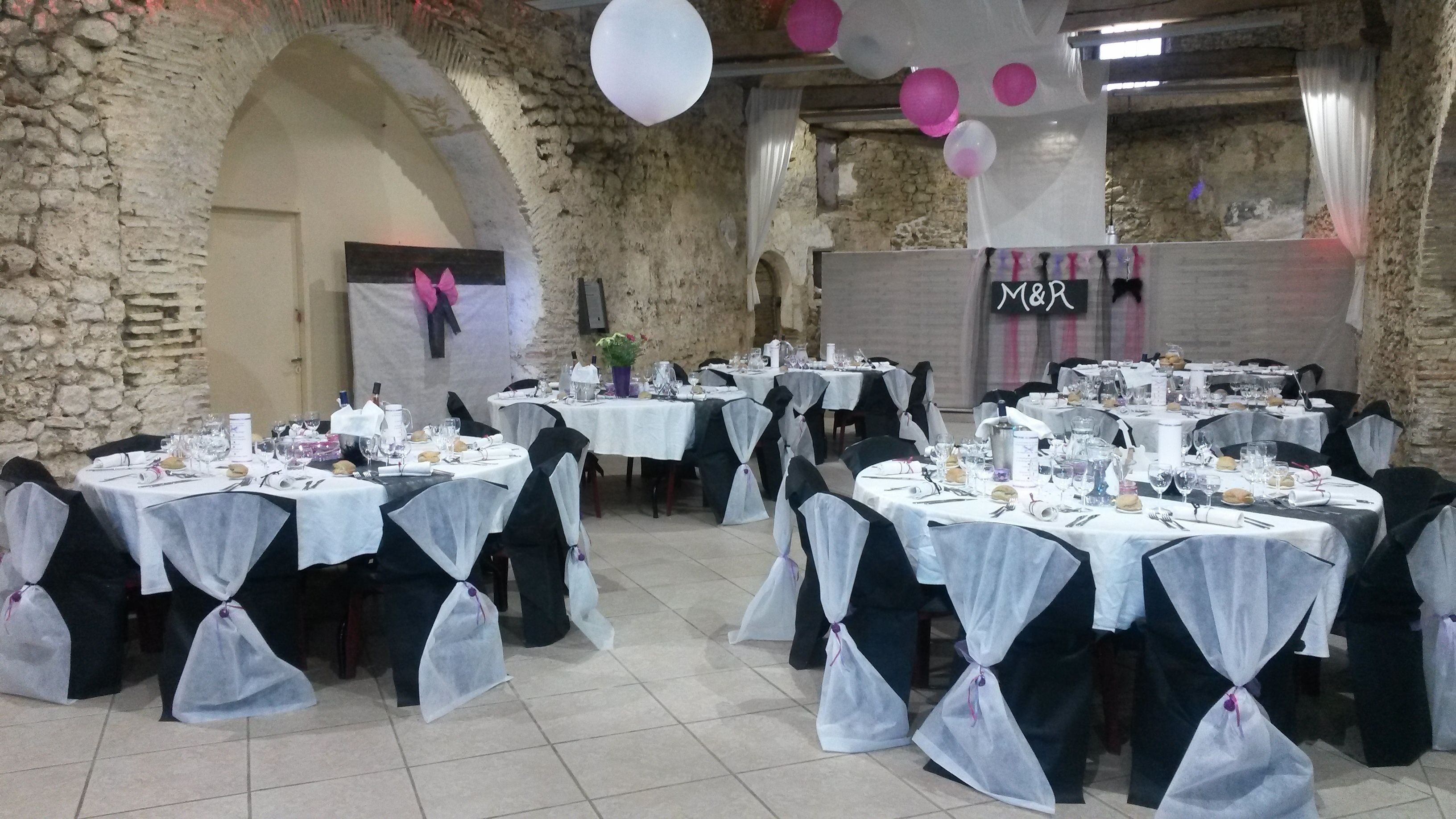 Una sala de banquetes amb diverses taules rodones preparades per a un esdeveniment formal, amb teles de taula blanques i cadires negres amb lligams blancs.