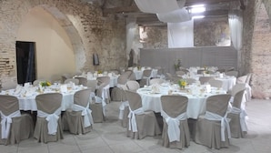 A banquet hall with round tables set for a formal event, featuring white tablecloths and beige chairs.