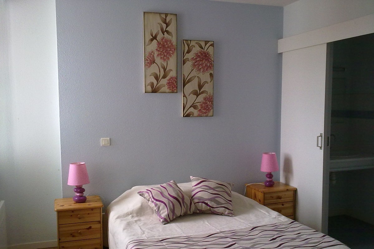 A bedroom with a bed, two nightstands, a dresser, and two wall-mounted lamps.
