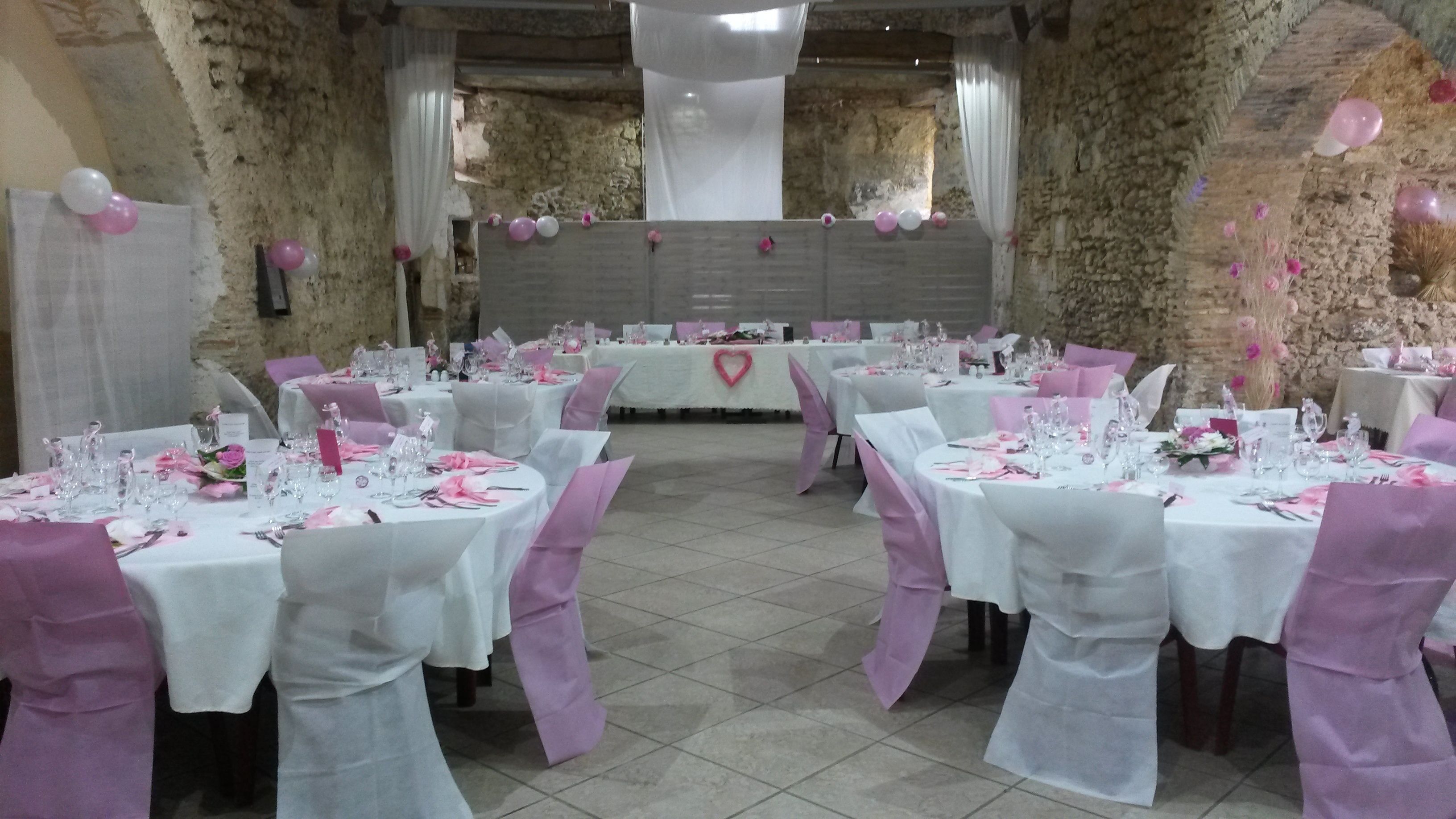 A banquet hall with round tables set for a formal event, featuring white tablecloths and pink accents.