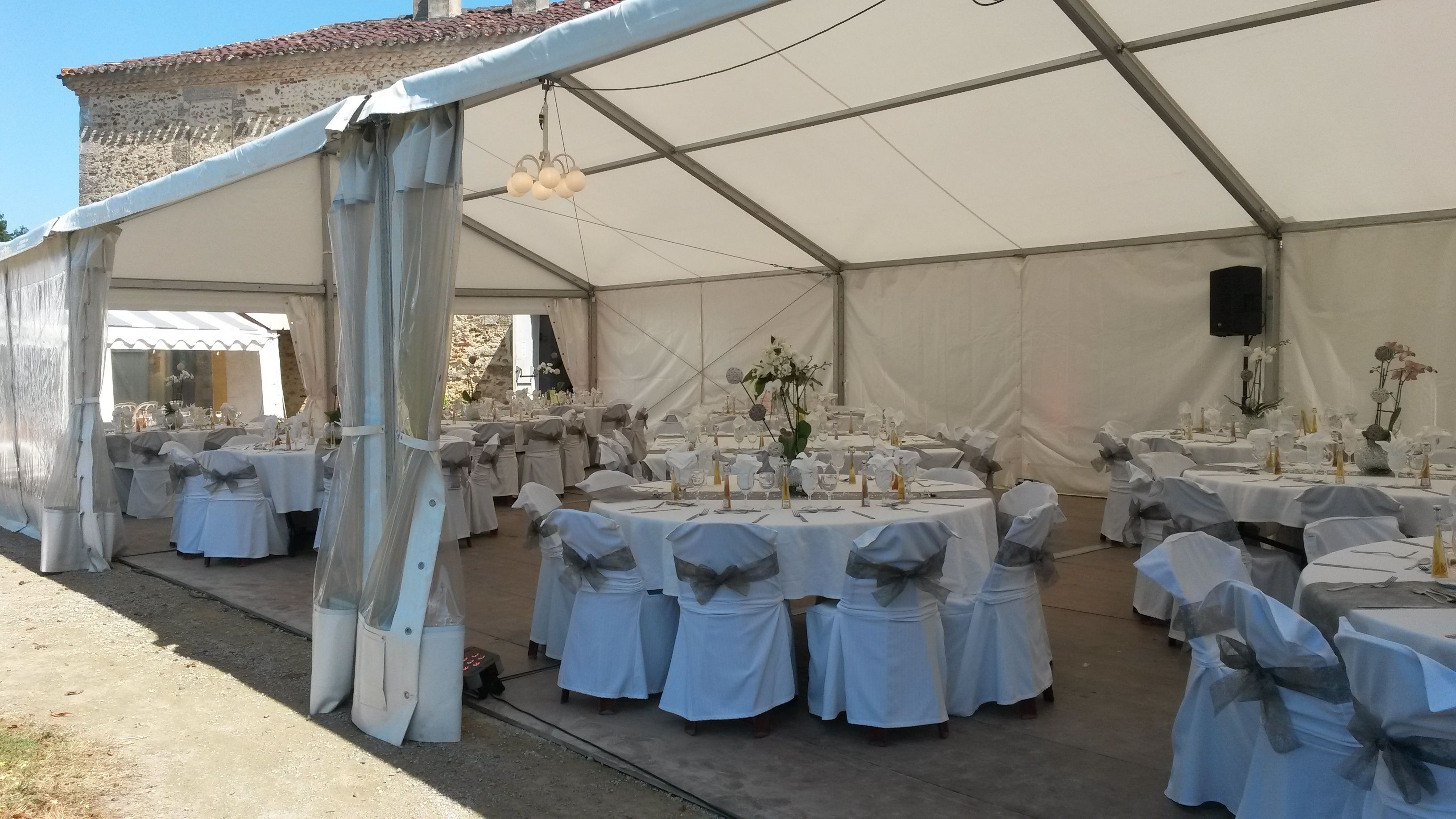 A tented event space with round tables set for dining, each with white tablecloths and chairs tied with grey sashes.