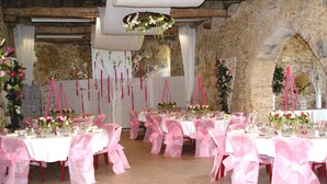 A banquet hall with multiple tables set for a formal event, featuring white tablecloths and pink chair covers.