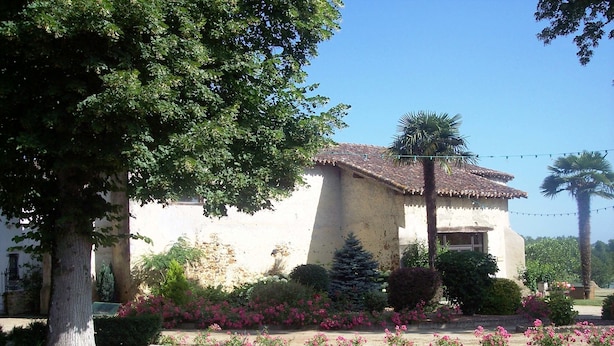 A house with a tiled roof, surrounded by a well-maintained garden with flowering plants and a lawn.