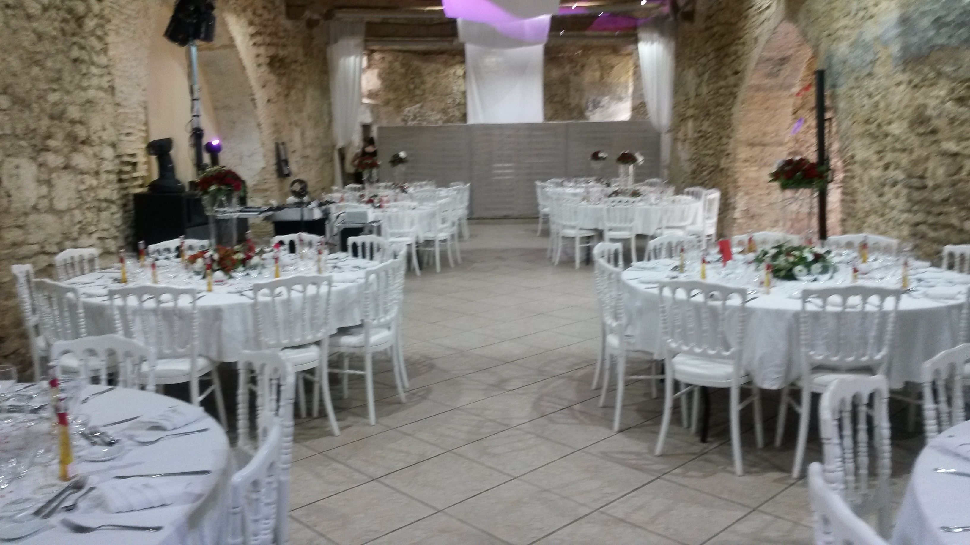 Un salón de banquetes con mesas redondas dispuestas para cenar, sillas blancas y un fondo de pared de piedra.