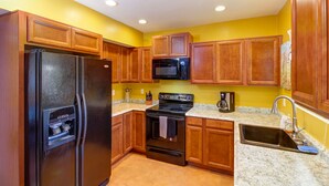 Una cocina con armarios de madera, un refrigerador negro, un microondas, una estufa y un lavamanos.