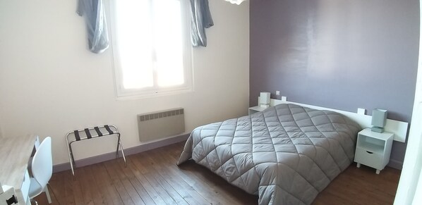 A bedroom with a bed, a chair, a nightstand, a radiator, and a window with curtains.