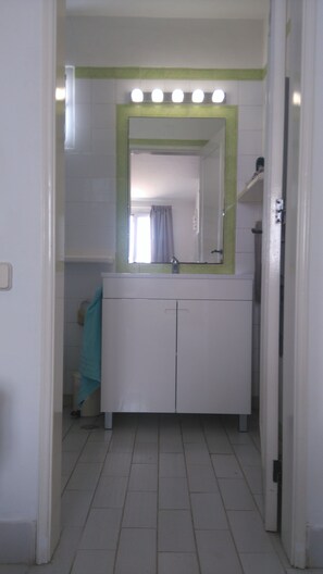 Ein Badezimmer mit weißem Waschtisch, einem Spiegel mit grünem Rahmen und einem Handtuch an der Wand.