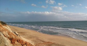 Ein Küstenstrand mit Wellen, blauem Himmel und einer Klippe.