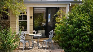 A patio with two metal chairs and a table, surrounded by greenery and a house with a sliding glass door.