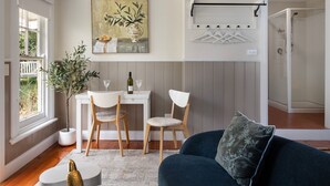 A modern living room with a dining area, a sofa, a coffee table, a painting, a plant, and a glass of wine on the table.