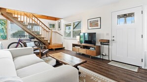 A living room with a wooden staircase, a sofa, a coffee table, a TV, and a bike.