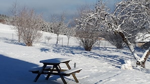A snow-covered picnic table in a park with bare trees and a fence in the background.