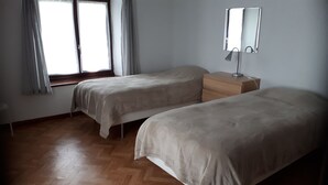 A bedroom with two beds, a wooden dresser, a mirror, and a window with curtains.