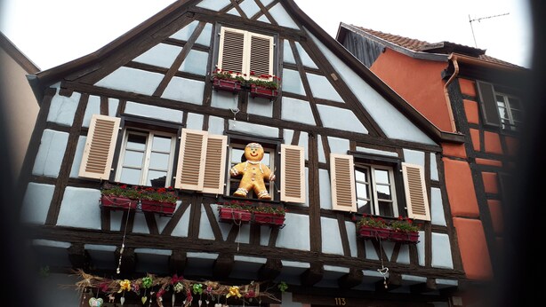 A half-timbered building with a gingerbread man decoration, flower boxes, and a number '113' visible.