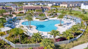A large, kidney-shaped swimming pool surrounded by palm trees and lounge chairs, with a view of residential buildings in the background. - Epic Star Wars & Disney Retreat Near Theme Parks (Kissimmee)