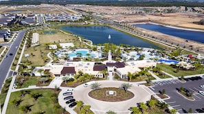An aerial view of a residential area with a central swimming pool, multiple buildings, and a large parking lot.
