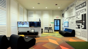 A modern waiting area with a colorful geometric carpet, black seating, a reception desk with a computer, and a wall decorated with black and white illustrations. - Epic Star Wars & Disney Retreat Near Theme Parks (Kissimmee)