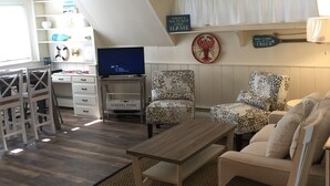 Una sala de estar acogedora con ventilador de techo, televisor, una mesa de centro y dos sillones estampados de leopardo.