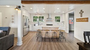A modern kitchen with a central island, bar stools, and a cross on the wall.