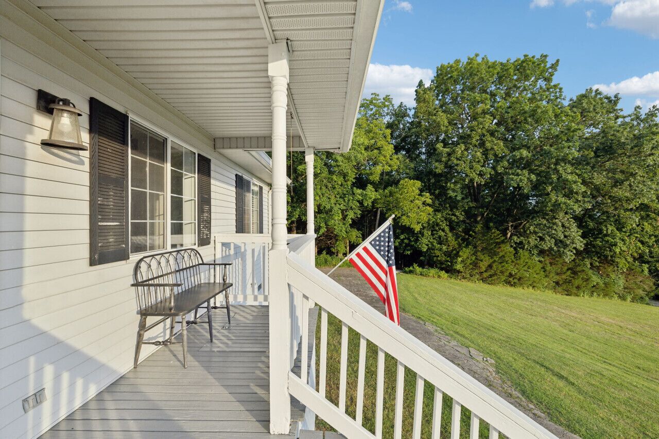 A porch with a bench, an American flag, and a white railing.