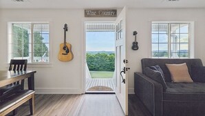 A room with a wooden dining table, a dark-colored sofa, and a door leading to a balcony with a view of greenery and hills.