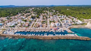 An aerial view of a coastal town with a marina, residential buildings, and a rocky breakwater. - House in Mallorca Ca Sa Tati near the beach (Son Serra de Marina)
