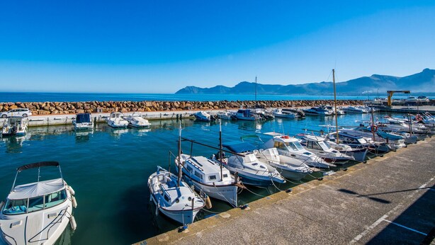 A marina with boats docked along a rocky breakwater, a clear sky, and mountains in the distance. - House in Mallorca Ca Sa Tati near the beach (Son Serra de Marina)