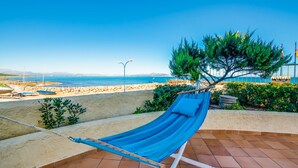 A hammock on a tiled patio overlooking a beach with boats and a clear sky. - House in Mallorca Ca Sa Tati near the beach (Son Serra de Marina)