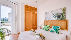 A hotel room with a bed, a wooden headboard, a painting, a bedside table with a lamp, and a view of the outdoors. - House in Mallorca Ca Sa Tati near the beach (Son Serra de Marina)
