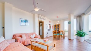 A living room with a sofa, a coffee table, a dining table with chairs, a ceiling fan, and a potted plant. - House in Mallorca Ca Sa Tati near the beach (Son Serra de Marina)