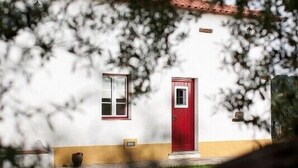 Un bâtiment blanc avec une porte et une fenêtre rouges, entouré d’arbres.