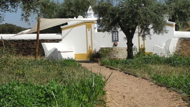 Un bâtiment blanc avec des ornements jaunes, un mur de pierre et un chemin qui y mène.