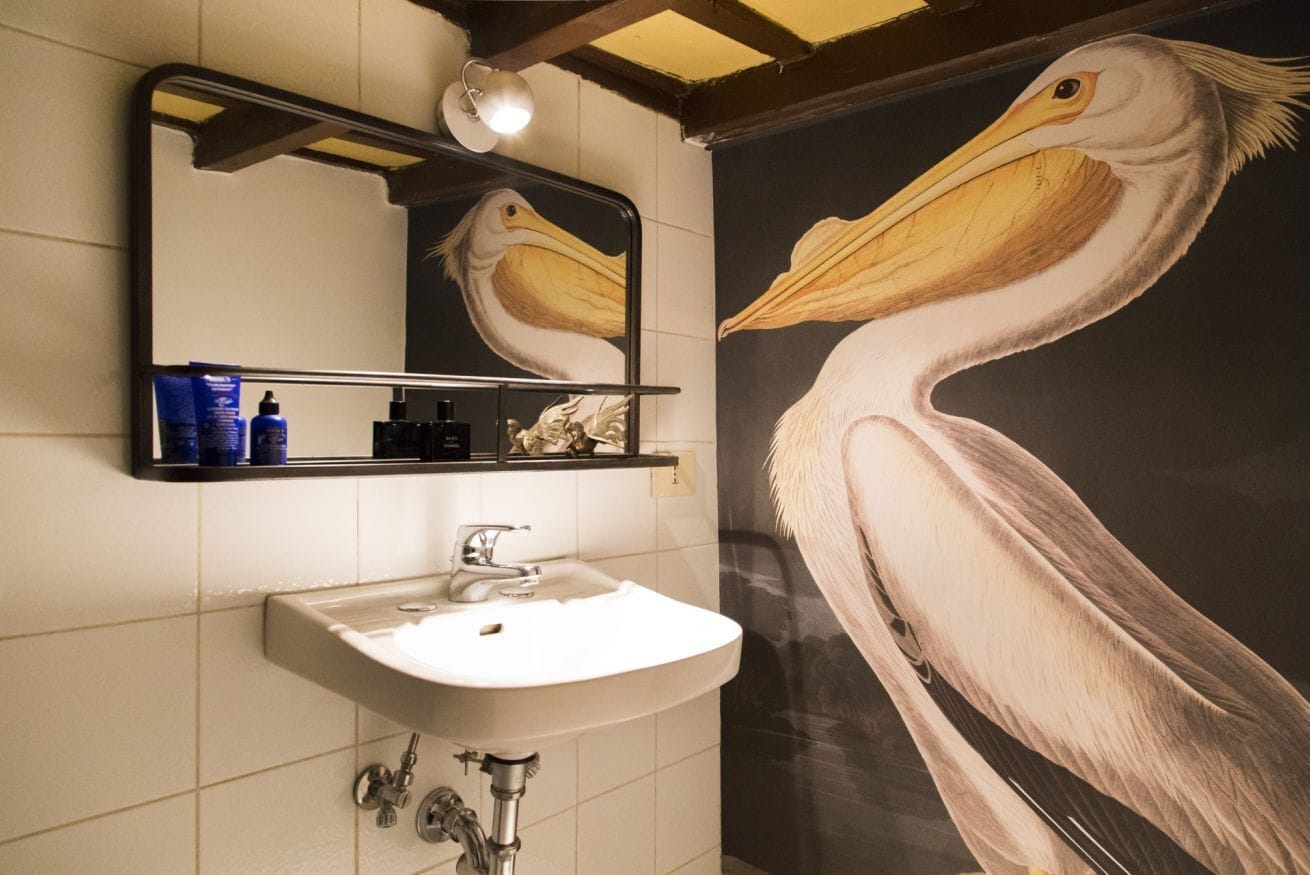 Een badkamer met een wastafel, spiegel en een groot pelikaan schilderij.