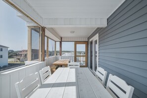 A covered porch with a table and chairs, large windows, and a view of the surrounding area. - 5233- Surfin' Shamrock, Family Beach Escape | Pool, Games & Cabana (Kill Devil Hills)