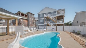 En swimmingpool med vandrutsjebaner, omgivet af et hegn med liggestole og en høj bygning i baggrunden.