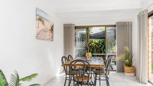 Un coin repas avec une table et des chaises, un tableau au mur et une vue sur la verdure à travers une porte vitrée.