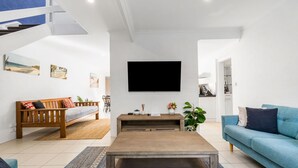 Un salon moderne avec un canapé en bois, un divan bleu, une table basse et un téléviseur à écran plat fixé au mur.