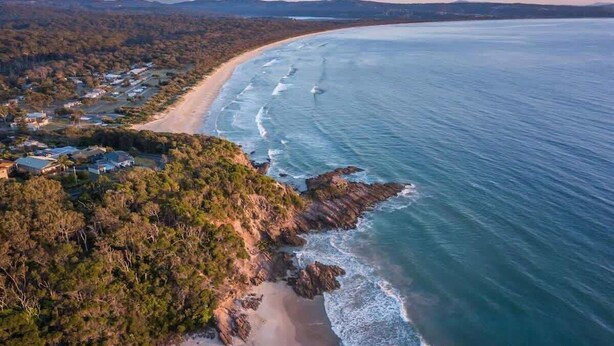 Vue aérienne d’une zone côtière avec une plage, des maisons et une végétation luxuriante.