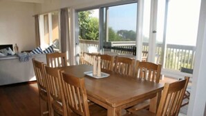 Un espace repas avec une table et des chaises en bois, de grandes fenêtres et une vue sur l’extérieur.