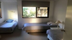 A bedroom with two single beds, a large window, and a bedside table with a lamp.